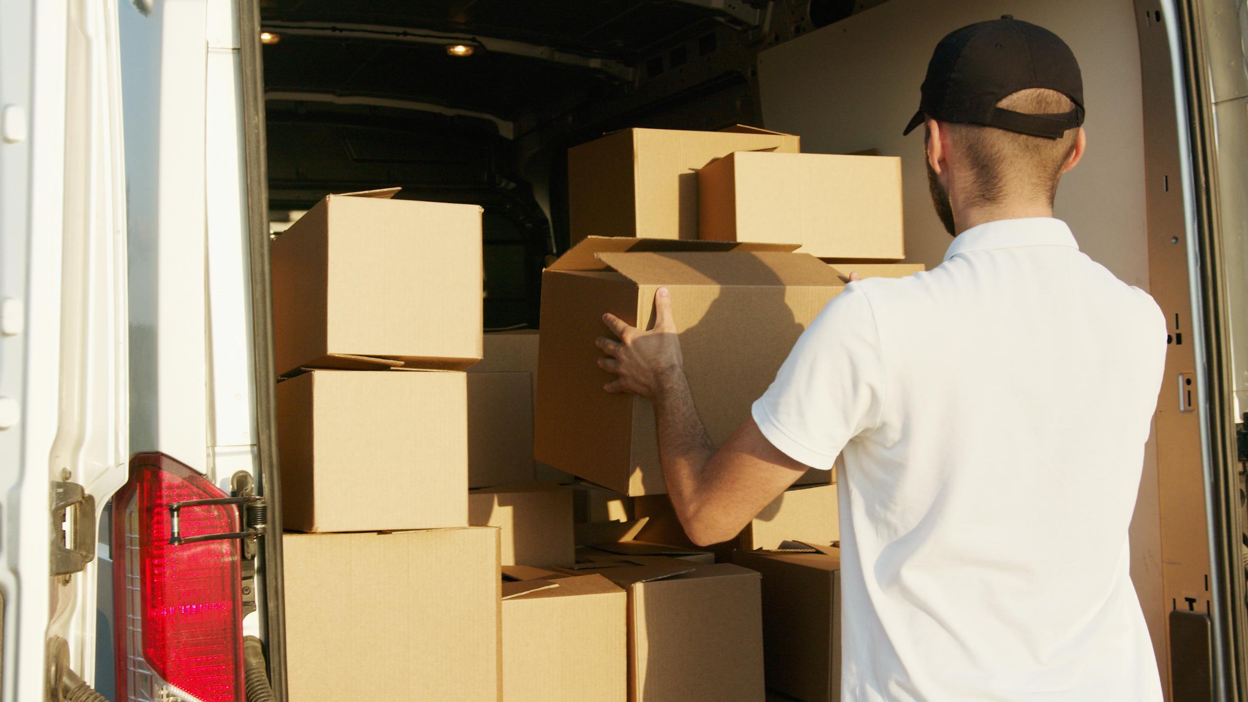 Courier arranging cardboard boxes in a delivery van during daytime.